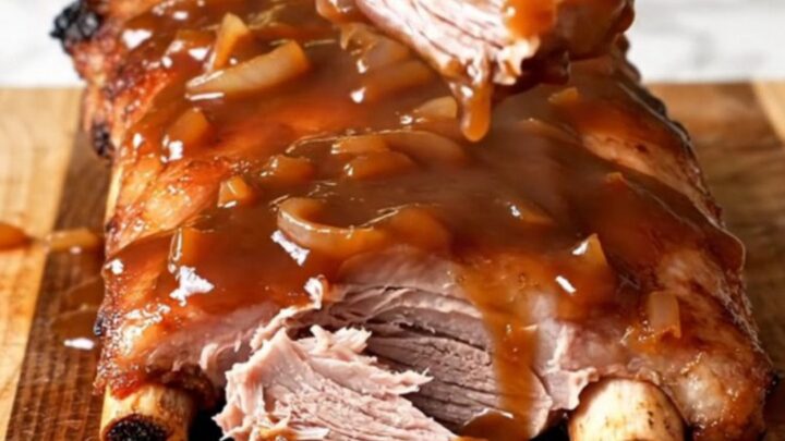 A close-up of tender, saucy country-style pork ribs in a slow cooker with visible onion slices.