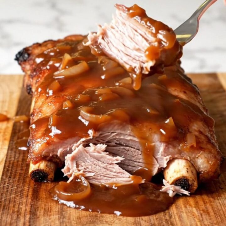 A close-up of tender, saucy country-style pork ribs in a slow cooker with visible onion slices.