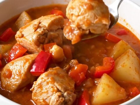 A top-down view of a black slow cooker insert filled with raw chicken, cubed potatoes, and peppers.