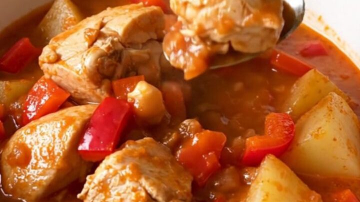 A top-down view of a black slow cooker insert filled with raw chicken, cubed potatoes, and peppers.