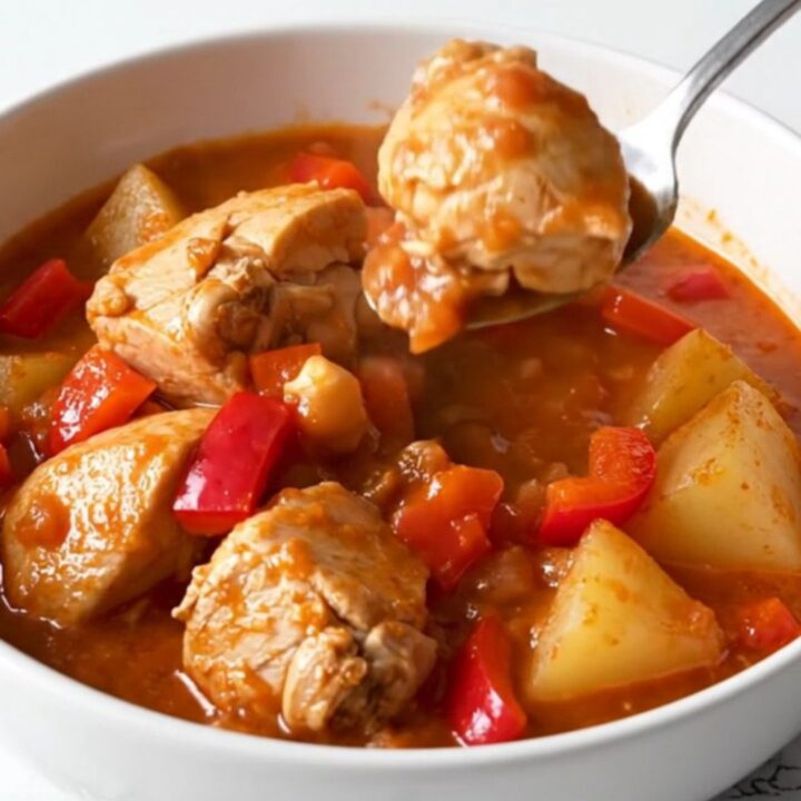 A top-down view of a black slow cooker insert filled with raw chicken, cubed potatoes, and peppers.