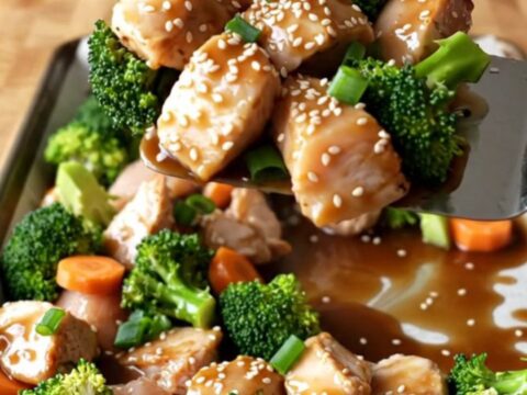 A sheet pan filled with golden-brown chicken chunks, vibrant broccoli, and carrot coins glazed in a savory ginger sauce.