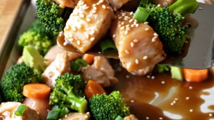 A sheet pan filled with golden-brown chicken chunks, vibrant broccoli, and carrot coins glazed in a savory ginger sauce.