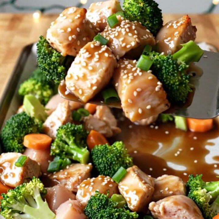 A sheet pan filled with golden-brown chicken chunks, vibrant broccoli, and carrot coins glazed in a savory ginger sauce.