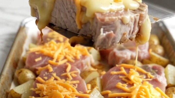 A sheet pan filled with golden roasted pork chops and baby potatoes topped with melted cheddar cheese.
