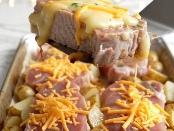 A sheet pan filled with golden roasted pork chops and baby potatoes topped with melted cheddar cheese.