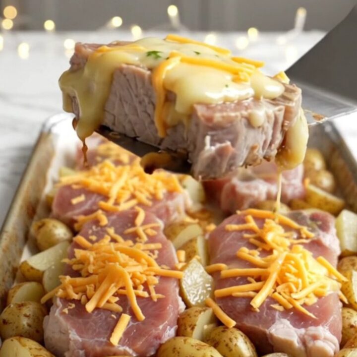 A sheet pan filled with golden roasted pork chops and baby potatoes topped with melted cheddar cheese.