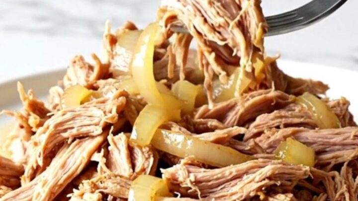 A close-up of tender, shredded pulled pork in a slow cooker with red onions and lemon-infused juices.