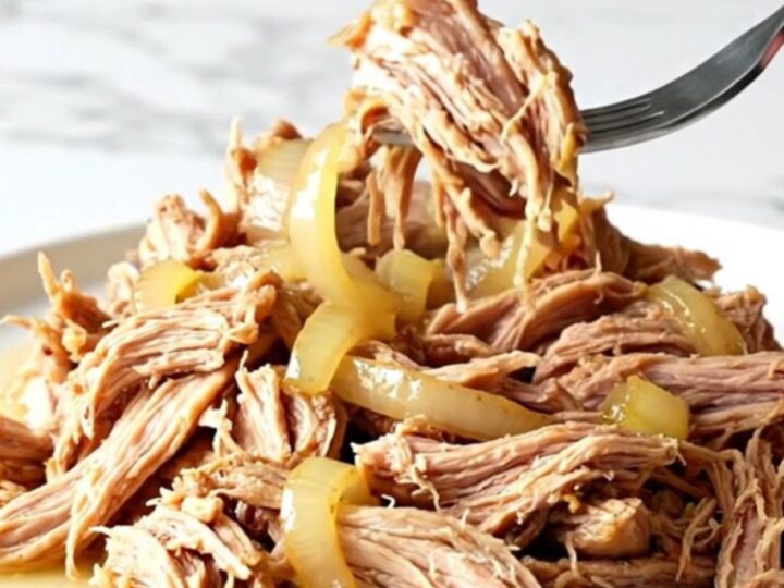 A close-up of tender, shredded pulled pork in a slow cooker with red onions and lemon-infused juices.