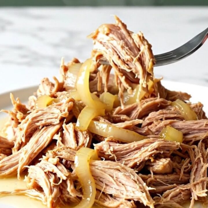 A close-up of tender, shredded pulled pork in a slow cooker with red onions and lemon-infused juices.