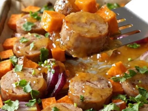A sheet pan filled with roasted chicken sausage coins, golden sweet potato cubes, and tender red onion wedges.