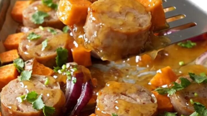 A sheet pan filled with roasted chicken sausage coins, golden sweet potato cubes, and tender red onion wedges.