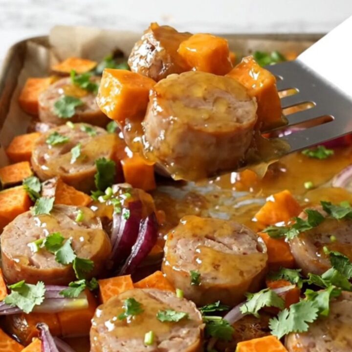 A sheet pan filled with roasted chicken sausage coins, golden sweet potato cubes, and tender red onion wedges.