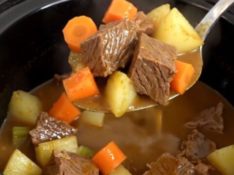 A close-up of beef pot roast potato soup in a black slow cooker insert, showing tender beef and vegetables.