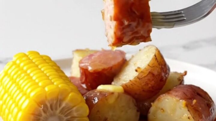 A slow cooker filled with sliced kielbasa, corn cobs, and red potatoes ready to be cooked.