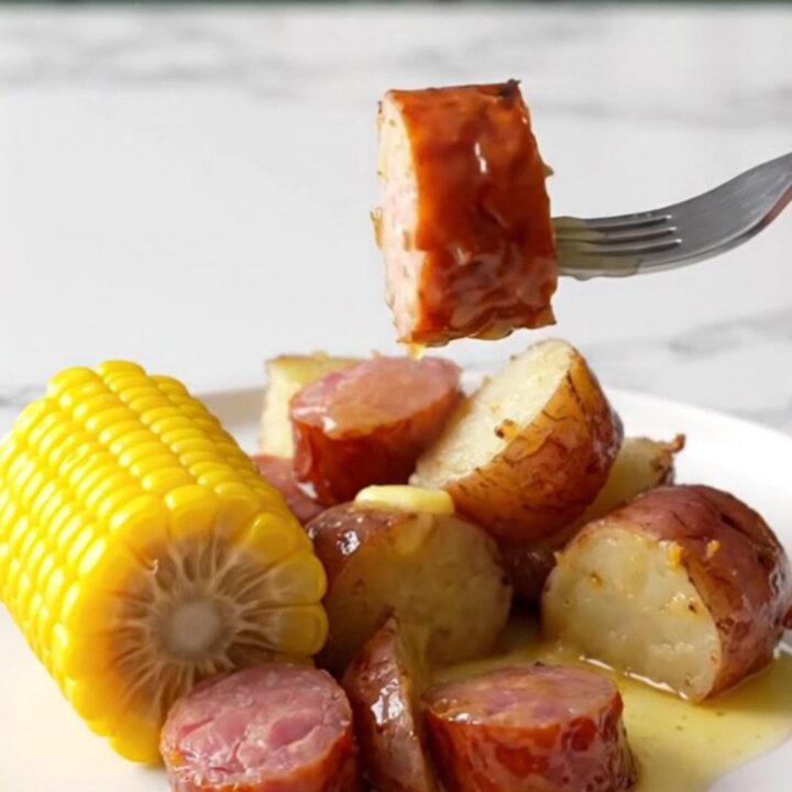 A slow cooker filled with sliced kielbasa, corn cobs, and red potatoes ready to be cooked.
