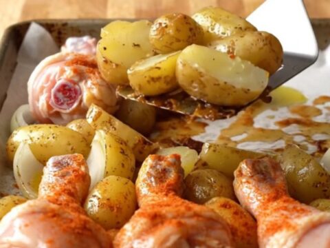 Crispy golden-brown chicken drumsticks roasted on a sheet pan with baby potatoes and onions.