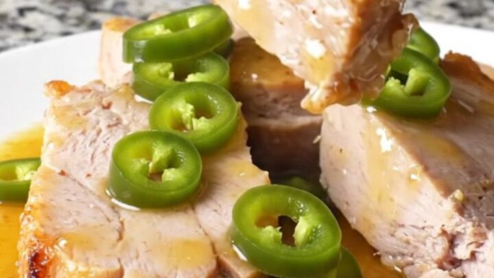 Two pork tenderloins sitting in a slow cooker with peach preserves and jalapeños.