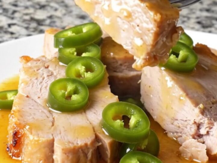 Two pork tenderloins sitting in a slow cooker with peach preserves and jalapeños.
