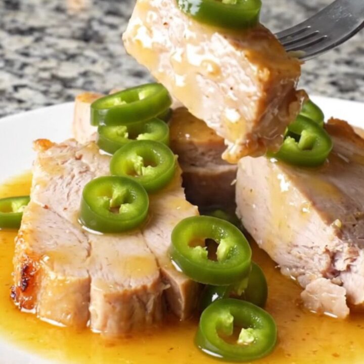 Two pork tenderloins sitting in a slow cooker with peach preserves and jalapeños.
