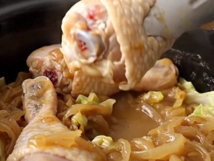 Slow cooker filled with chicken drumsticks and cabbage wedges in a savory onion sauce.