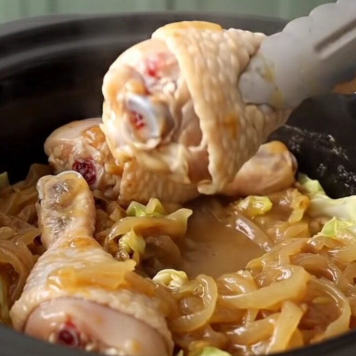 Slow cooker filled with chicken drumsticks and cabbage wedges in a savory onion sauce.