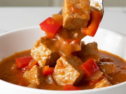 A bowl of steaming Hungarian pork goulash with tender pork cubes in a rich, brick-red paprika sauce.