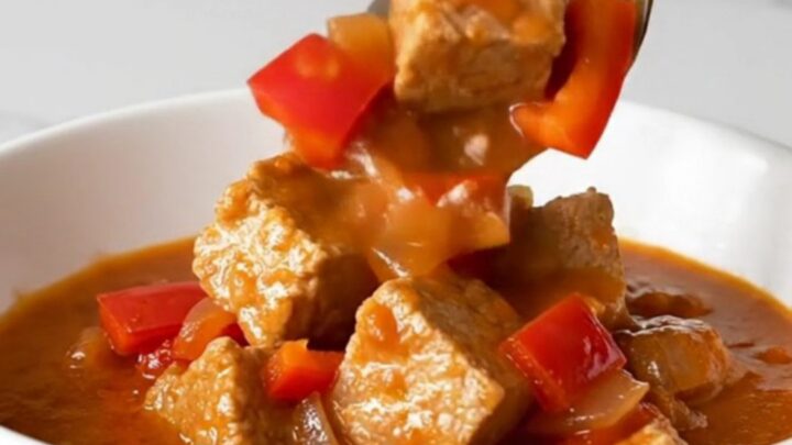 A bowl of steaming Hungarian pork goulash with tender pork cubes in a rich, brick-red paprika sauce.