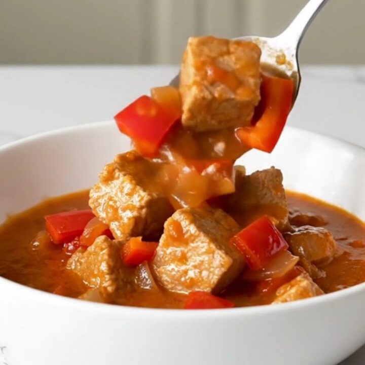 A bowl of steaming Hungarian pork goulash with tender pork cubes in a rich, brick-red paprika sauce.