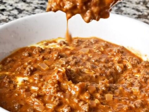 A warm, creamy reddish-brown Cincinnati chili dip in a white bowl with beef crumbles and visible spices.