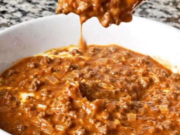 A warm, creamy reddish-brown Cincinnati chili dip in a white bowl with beef crumbles and visible spices.