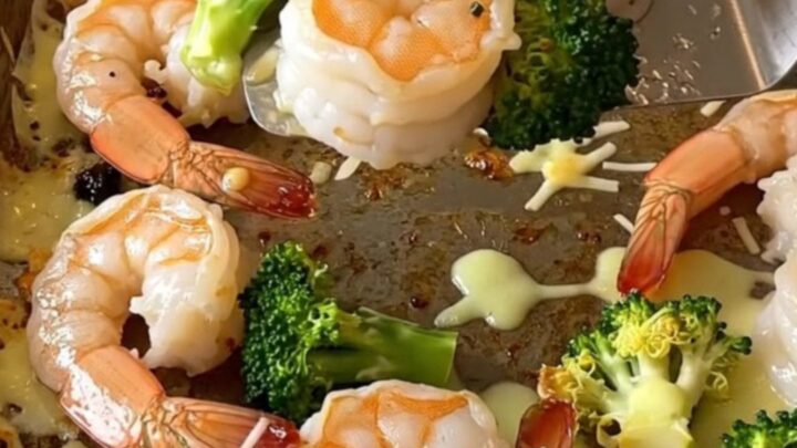A top-down view of a sheet pan filled with roasted shrimp and broccoli topped with golden melted parmesan.