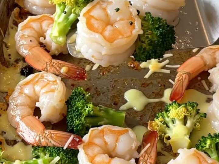 A top-down view of a sheet pan filled with roasted shrimp and broccoli topped with golden melted parmesan.