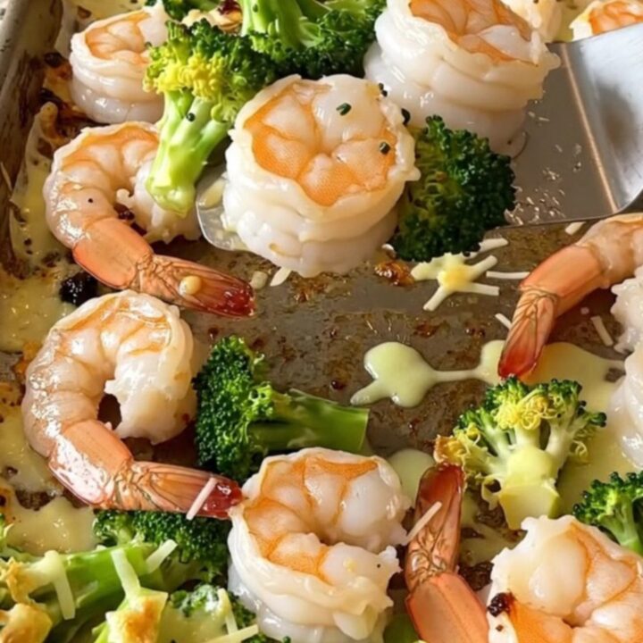 A top-down view of a sheet pan filled with roasted shrimp and broccoli topped with golden melted parmesan.