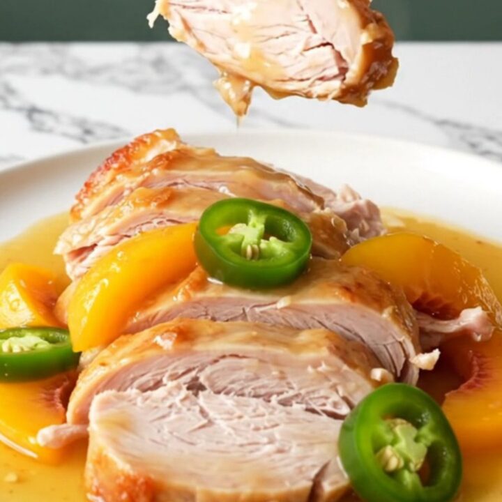 A whole boneless turkey breast cooking in a black slow cooker with peach slices and jalapeños.