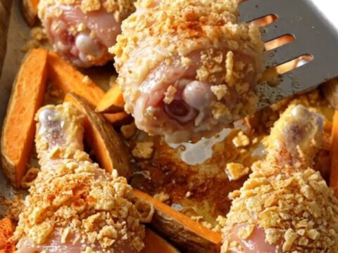 A sheet pan filled with golden cornflake-crusted chicken drumsticks and roasted sweet potato wedges.