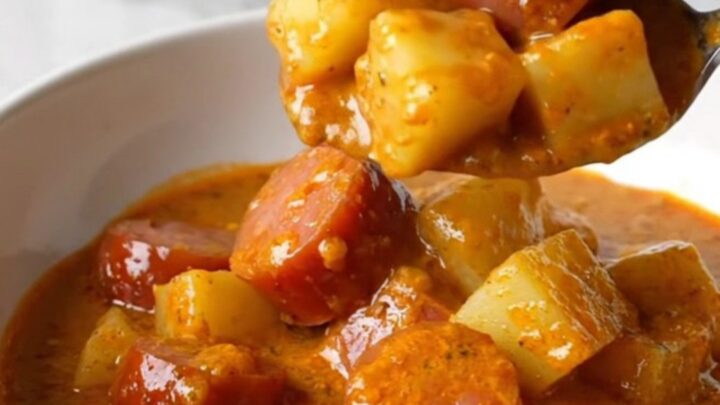 A white bowl filled with creamy Hungarian kielbasa paprikash, showing tender potato cubes and sliced sausage in an orange-red