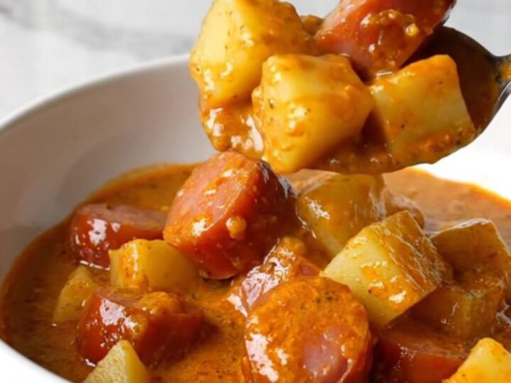 A white bowl filled with creamy Hungarian kielbasa paprikash, showing tender potato cubes and sliced sausage in an orange-red