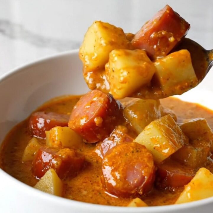 A white bowl filled with creamy Hungarian kielbasa paprikash, showing tender potato cubes and sliced sausage in an orange-red