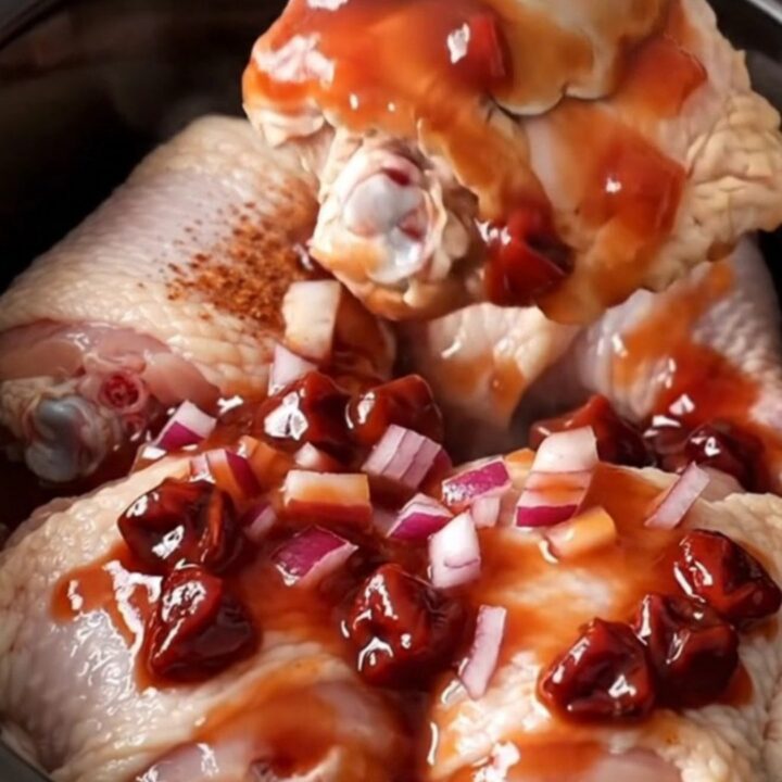 Slow cooker cherry chipotle chicken thighs with a rich dark red glaze served on a white plate.