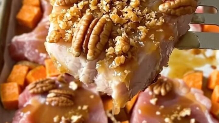 A sheet pan filled with golden-brown roasted pork chops and sweet potato cubes topped with crunchy chopped pecans.