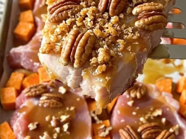A sheet pan filled with golden-brown roasted pork chops and sweet potato cubes topped with crunchy chopped pecans.