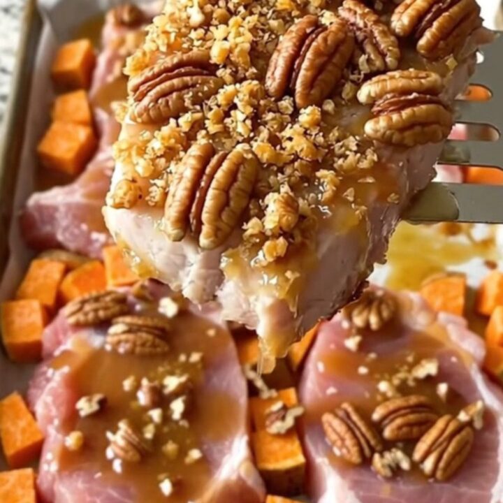 A sheet pan filled with golden-brown roasted pork chops and sweet potato cubes topped with crunchy chopped pecans.