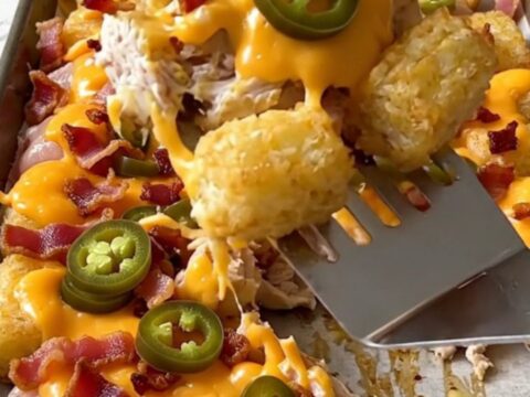 A sheet pan filled with crispy potato tots, cooked chicken chunks, melted cheddar, bacon, and jalapeno slices.