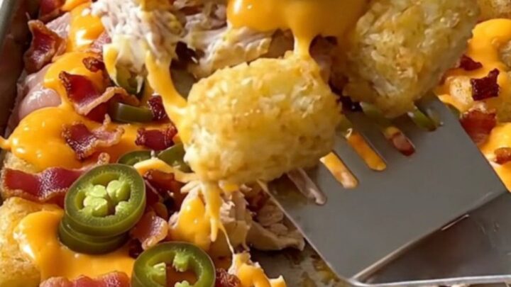 A sheet pan filled with crispy potato tots, cooked chicken chunks, melted cheddar, bacon, and jalapeno slices.