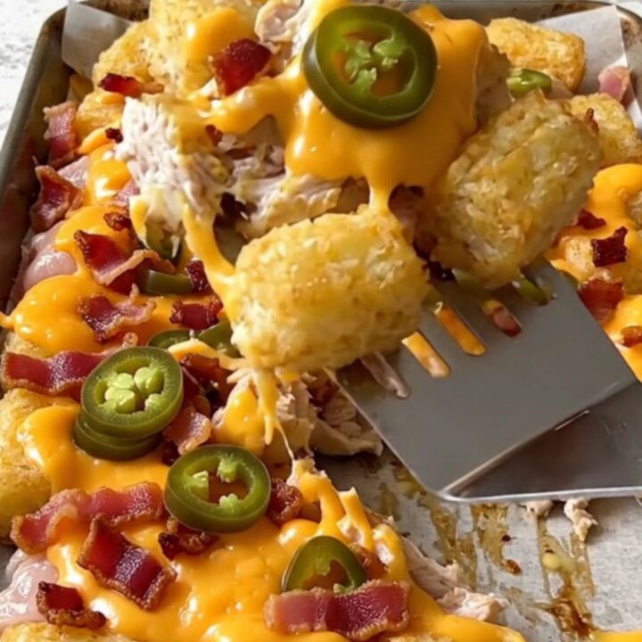 A sheet pan filled with crispy potato tots, cooked chicken chunks, melted cheddar, bacon, and jalapeno slices.