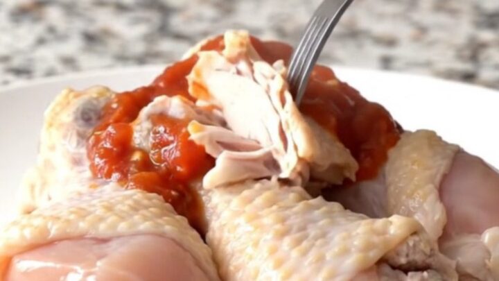 A close-up of slow-cooked chicken drumsticks with black beans and corn in a black stoneware insert.