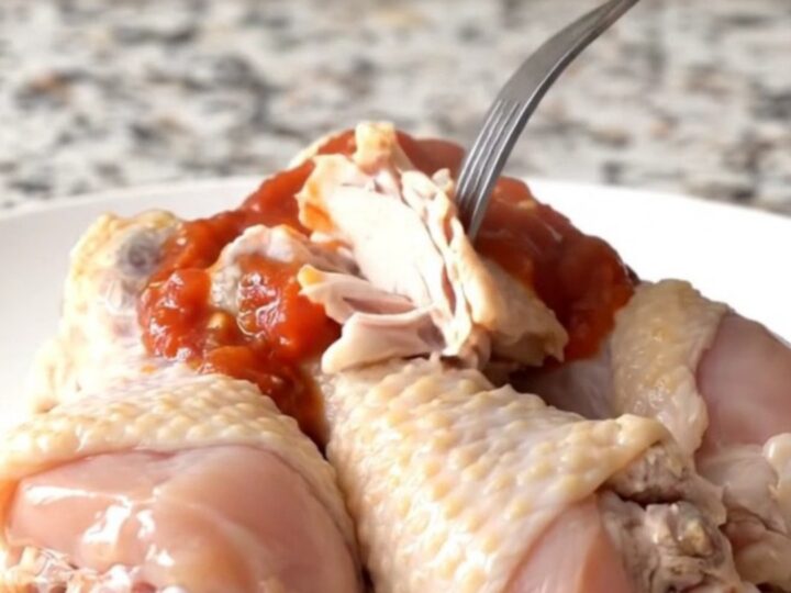 A close-up of slow-cooked chicken drumsticks with black beans and corn in a black stoneware insert.