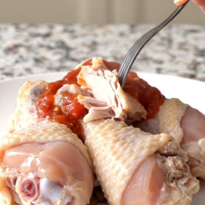 A close-up of slow-cooked chicken drumsticks with black beans and corn in a black stoneware insert.