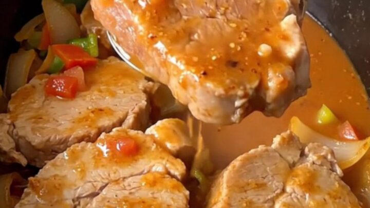 A close-up of tender, slow-cooked pork loin slices covered in a thick, savory vegetable gravy in a slow cooker.